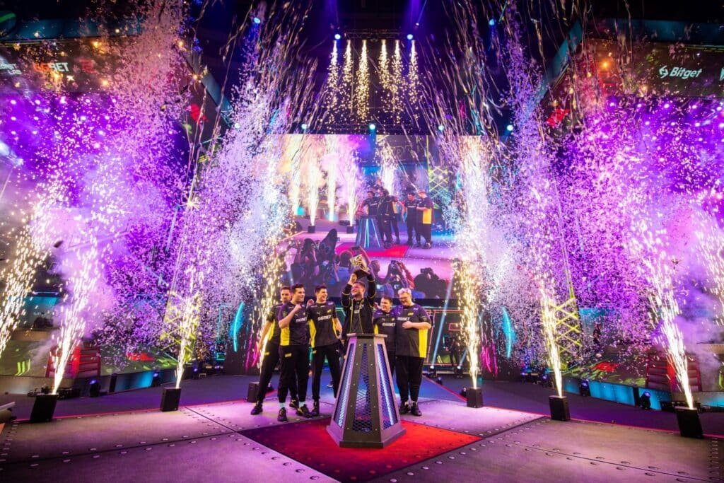 A imagem mostra a equipe de esportes Natus Vincere (NAVI) comemorando sua vitória no palco com o troféu e confetes no PGL Major Stockholm 2021.