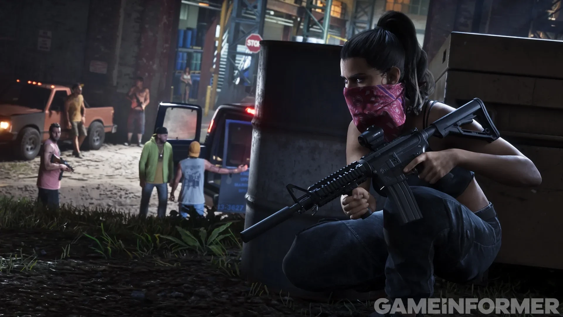 A protagonista de Grand Theft Auto VI, Lucia, se protegendo atrás de um contêiner segurando um rifle de assalto com uma bandana rosa no rosto, enquanto membros de uma gangue ficam perto de uma van em um beco industrial à noite.