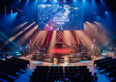 An esports stage for VALORANT Champions Paris with a large screen, red and blue lighting, and empty seating.