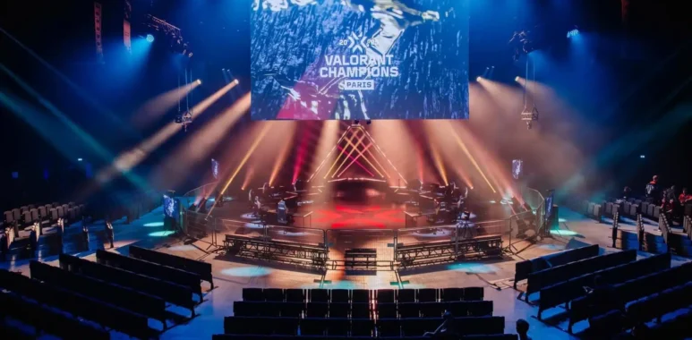 An esports stage for VALORANT Champions Paris with a large screen, red and blue lighting, and empty seating.