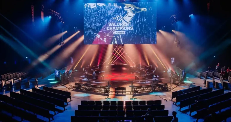 An esports stage for VALORANT Champions Paris with a large screen, red and blue lighting, and empty seating.