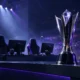 Esports championship trophy on a LAN stage with empty gaming chairs after a roster change