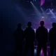 Five-player CS2 esports lineup silhouetted on a dark arena stage with one figure highlighted in violet
