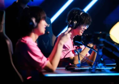 Two professional esports players in pink jerseys wearing headsets at a competition stage.