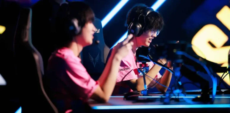 Two professional esports players in pink jerseys wearing headsets at a competition stage.