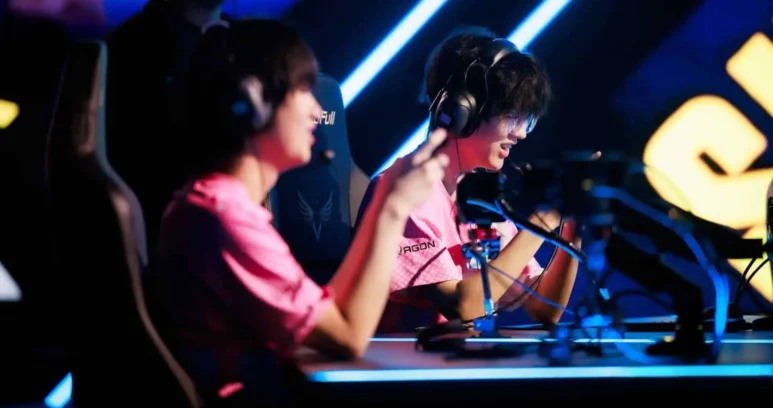 Two professional esports players in pink jerseys wearing headsets at a competition stage.