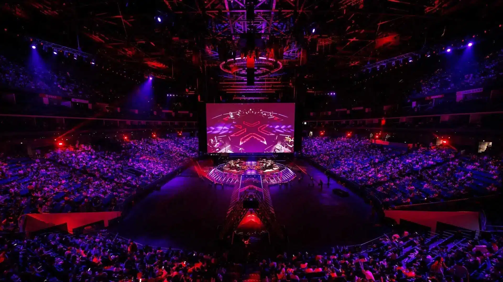 Plano geral do palco e do público da arena VALORANT Champions Shanghai sob iluminação vermelha e roxa.