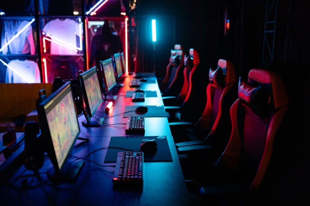 Fileira de PCs para jogos, teclados e cadeiras vermelhas para jogos sob iluminação neon