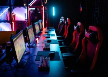 Row of gaming PCs, keyboards and red gaming chairs under neon lighting