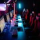 Row of gaming PCs, keyboards and red gaming chairs under neon lighting