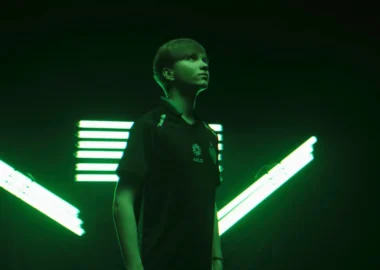 Portrait of Ilya "m0NESY" Osipov wearing a Team Falcons jersey against a green neon light background.