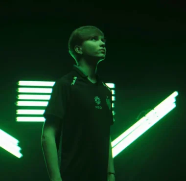 Portrait of Ilya "m0NESY" Osipov wearing a Team Falcons jersey against a green neon light background.