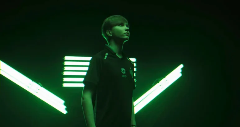Portrait of Ilya "m0NESY" Osipov wearing a Team Falcons jersey against a green neon light background.