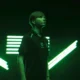Portrait of Ilya "m0NESY" Osipov wearing a Team Falcons jersey against a green neon light background.