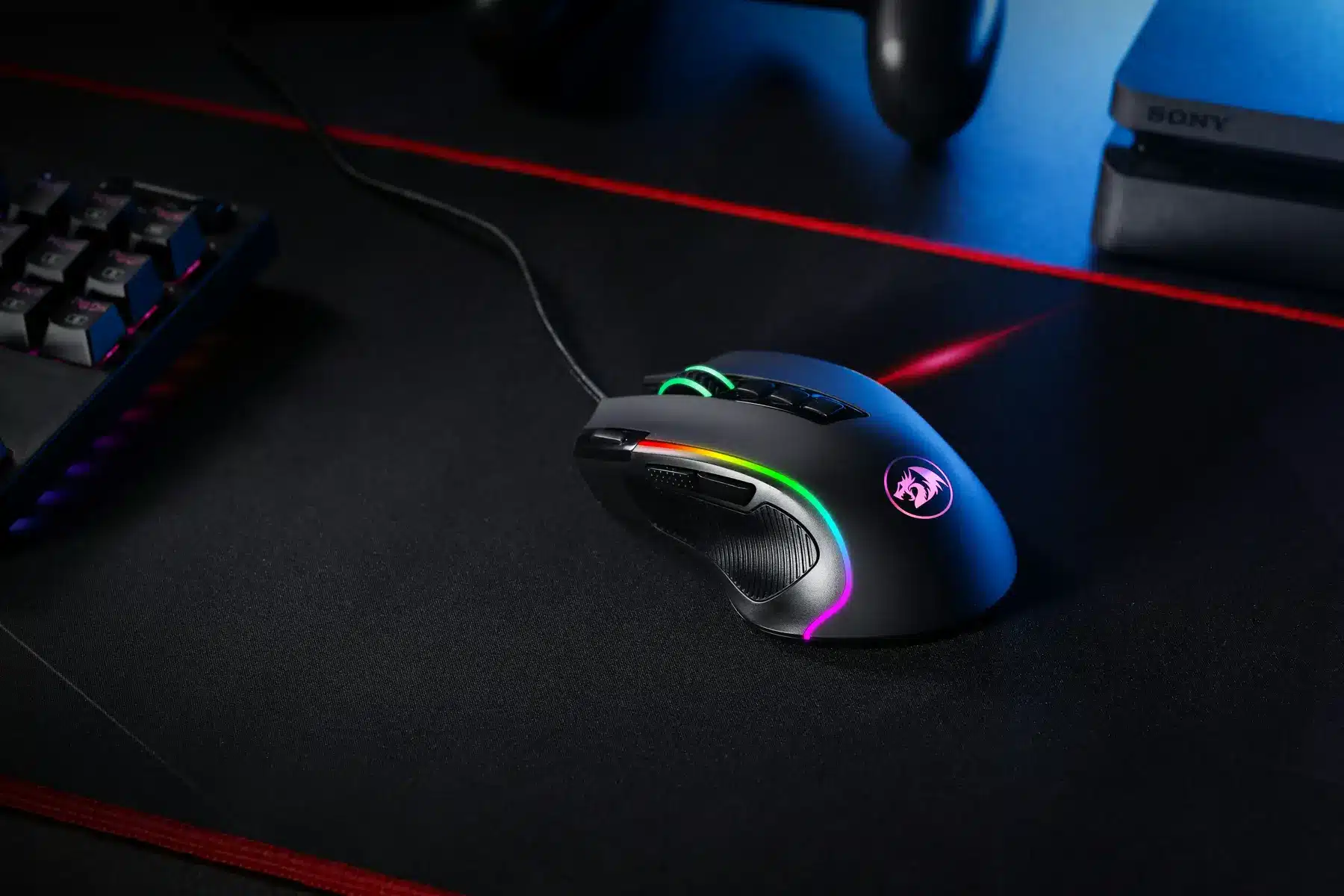 Um mouse para jogos preto com iluminação RGB em um mousepad preto próximo a um teclado